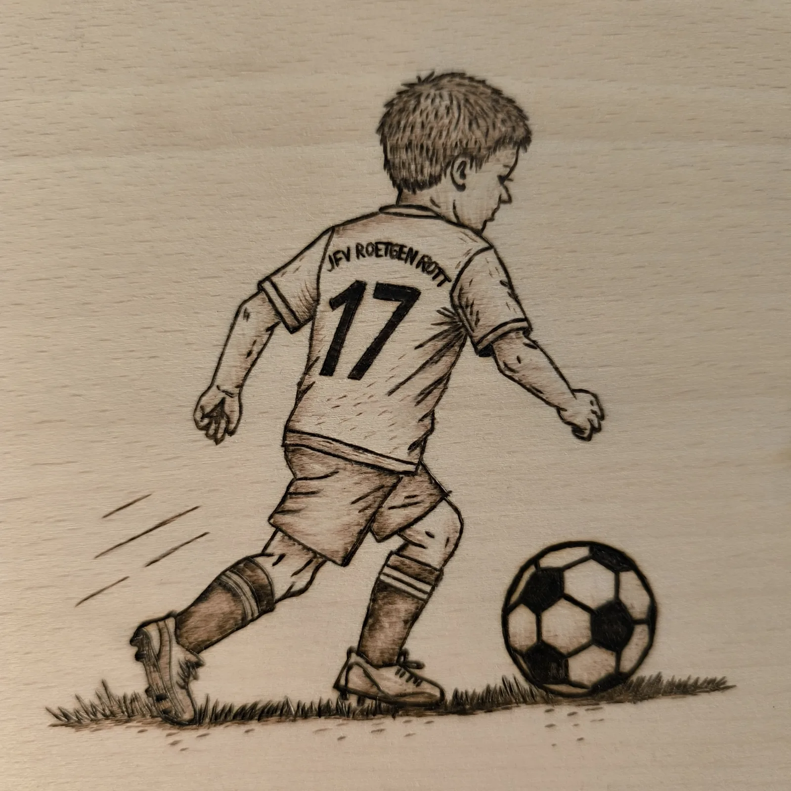 Detailansicht des Fußballspielers mit Trikotnummer 17 und Ball auf einem Buchenholzbrettchen.