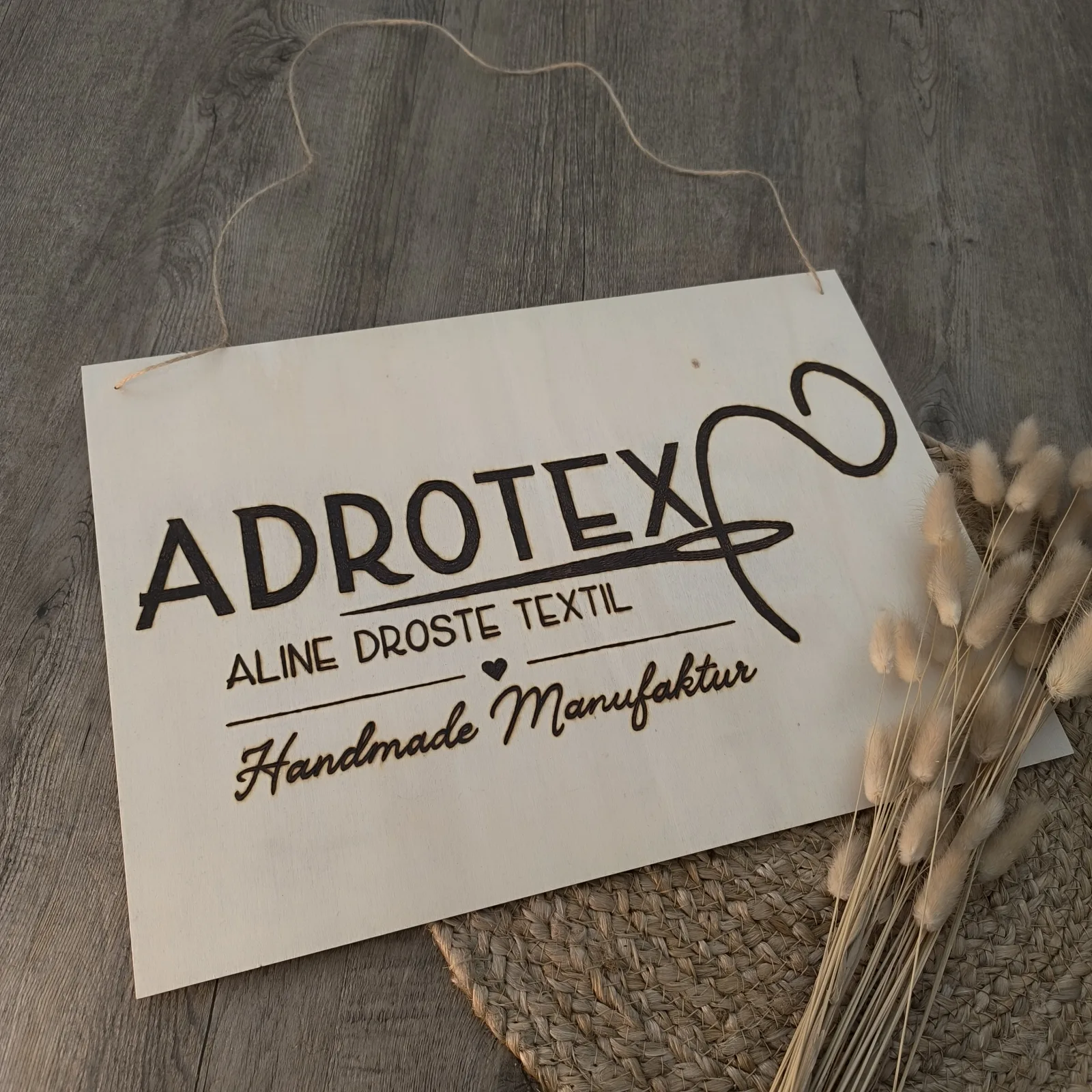 Hängendes Holzschild mit Firmenlogo ADROTEX und Aufschrift Aline Droste Textil.