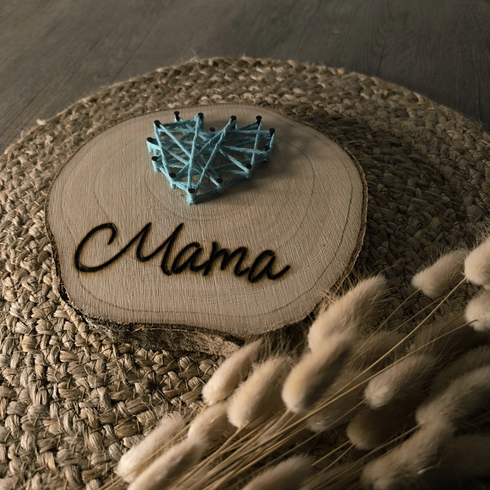 Holzscheibe mit blau gespanntem Herz aus Faden und der Aufschrift Mama.