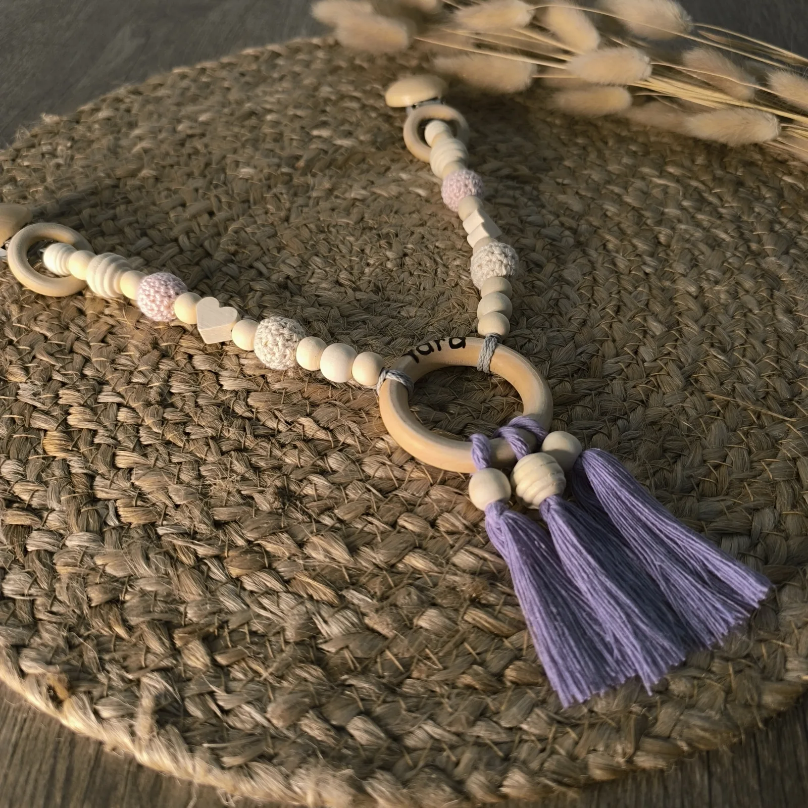 Kinderwagenkette aus Holzperlen mit Clips, Herzperle, Holzring und lila Makramee Quasten.