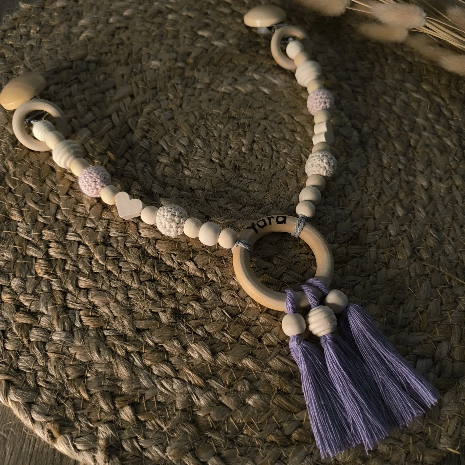 Kinderwagenkette aus Holzperlen mit Clips, Holzring, Trockenblumen und lila Makramee Quasten.
