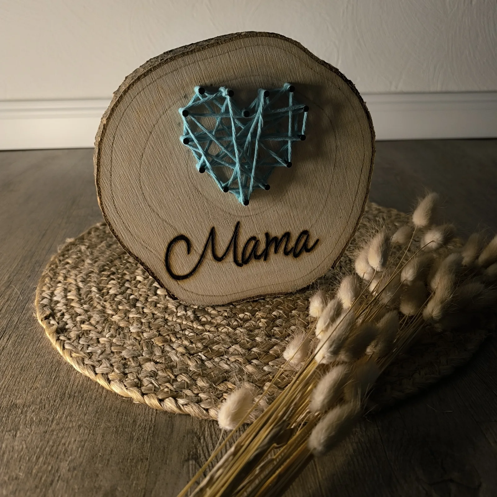 Runde Holzscheibe mit blauem Fadenherz und eingebrannter Aufschrift Mama.