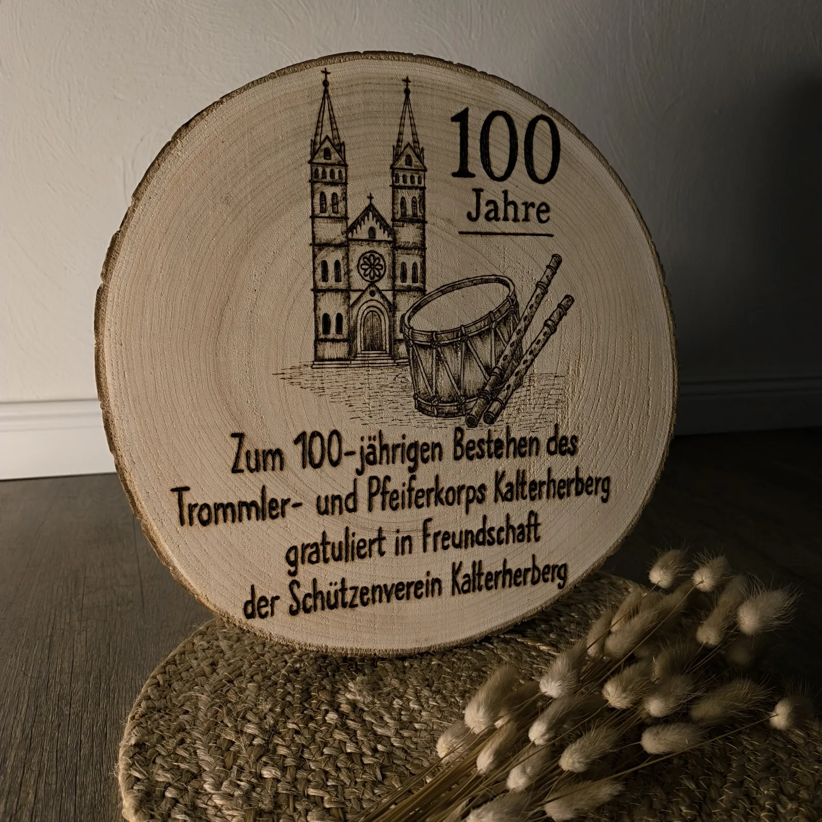 Runde Holzscheibe mit Jubiläumsaufschrift, Kirche, Trommel und Pfeifen auf Naturdeko.