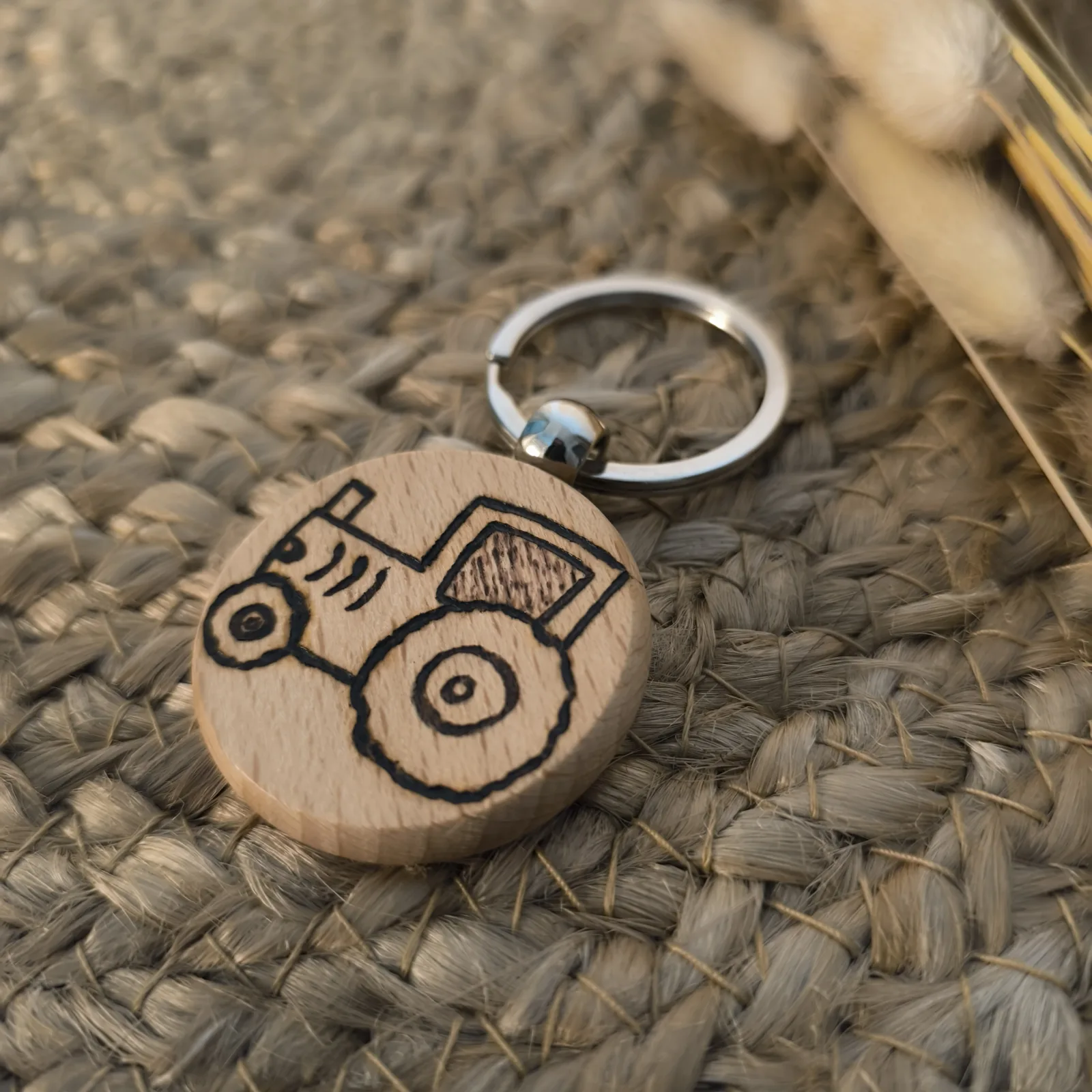 Runder Holz Schlüsselanhänger mit eingebranntem Traktor Motiv auf geflochtenem Untergrund.