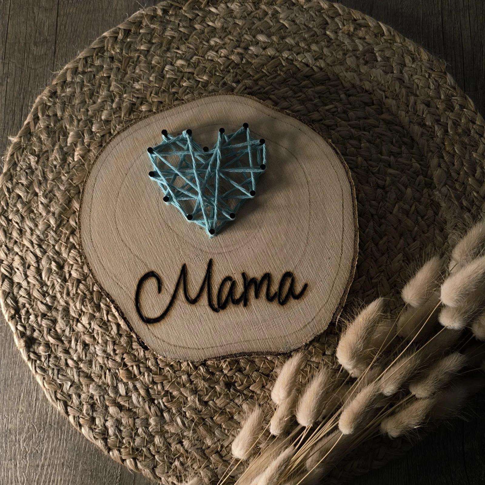 Seitliche Ansicht der Holzscheibe mit blauem Fadenherz und eingebrannter Aufschrift Mama.