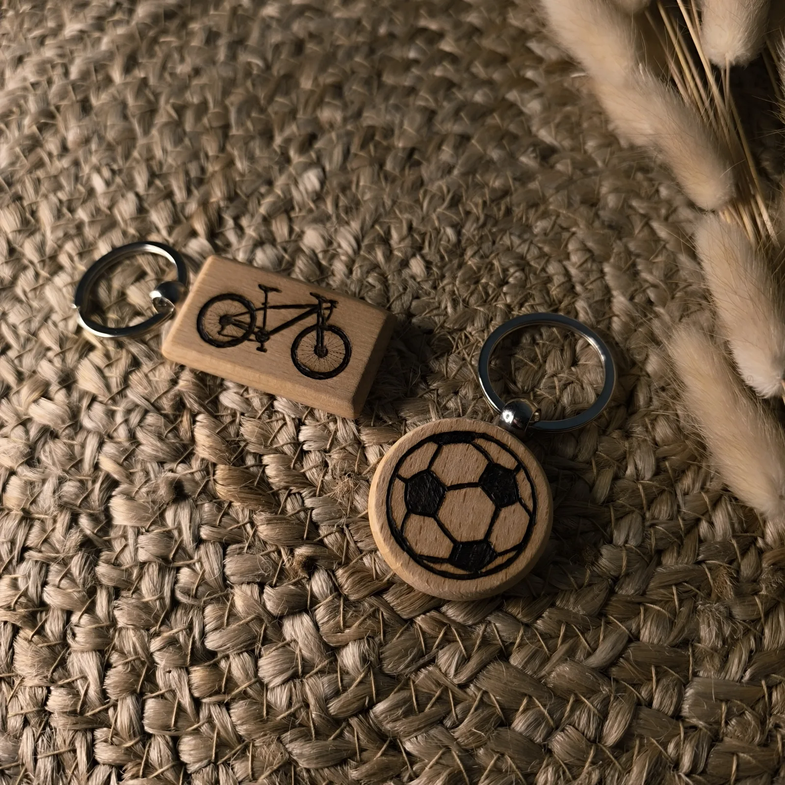 Zwei Holzschlüsselanhänger mit eingebranntem Fahrrad und Fußball als sportliche Motive.